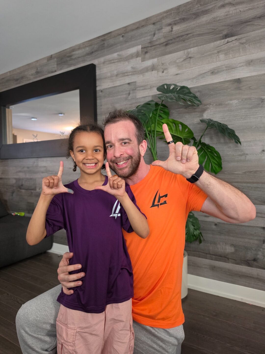 Ellyah et papa en t-shirts Looser Co. orange et violet, font le L avec leurs doigts